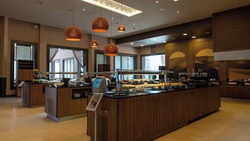 Une cuisine d’hôtel moderne dotée d’un îlot central servant de buffet, d’un éclairage suspendu et de grandes fenêtres.