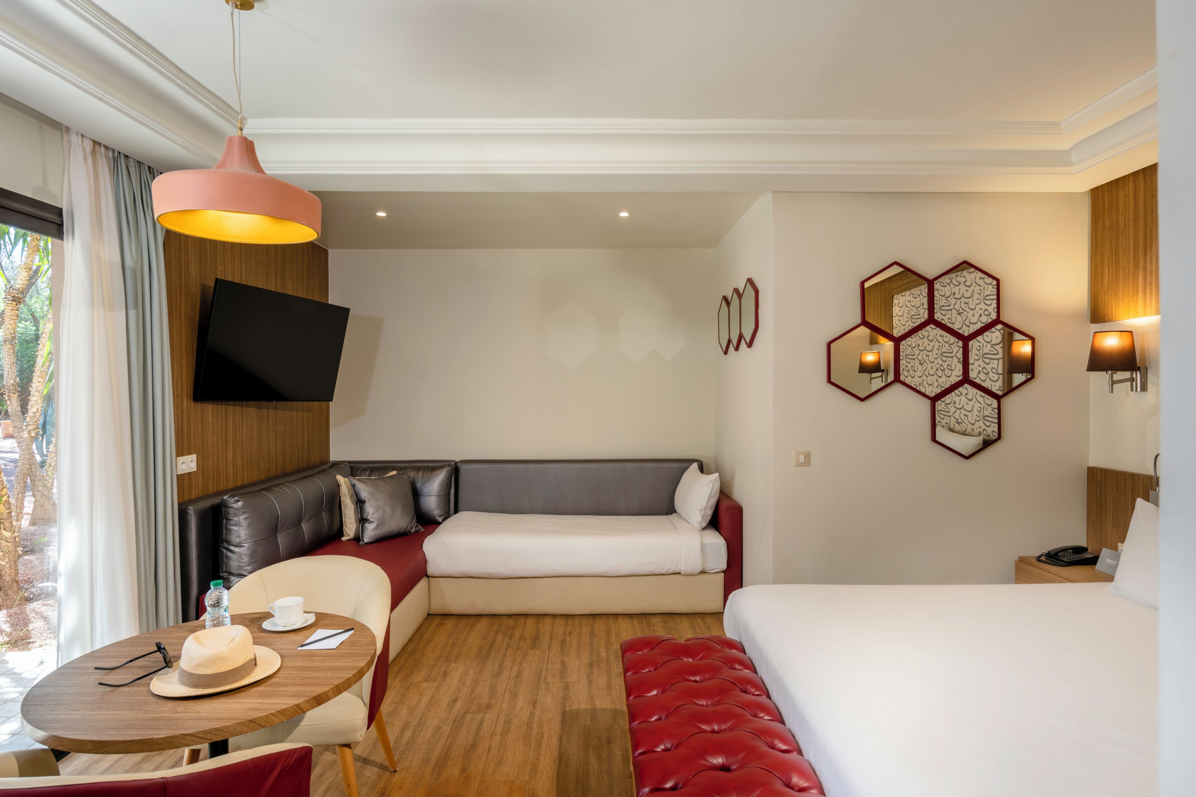 Ein Hotelzimmer mit einer Couch, einem Bett, einem Tisch mit Hut und Wasserflasche sowie einem an der Wand befestigten Fernseher.