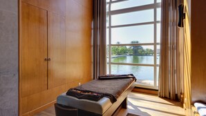 A massage room with a bench, wooden wardrobe, and a large window overlooking a lake.