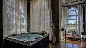 A spa room with a large soaking tub, a massage table, and a view of a garden through large windows.
