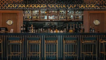 Un bar avec un décor mural à motifs, de nombreuses étagères remplies de bouteilles et des tabourets de bar.