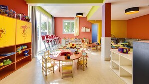 A brightly colored children's playroom with a large table, chairs, and shelves filled with toys.