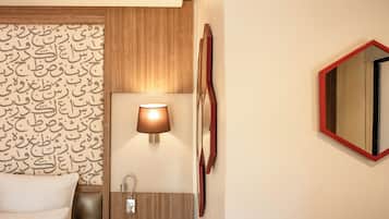Habitación de hotel con cama, lámpara de pared, espejo y panel de madera con escritura árabe.