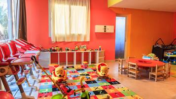A brightly colored children's playroom with a large window, a play mat with alphabet letters, and a small table with toys.