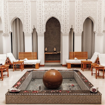 A luxurious spa room with a large central fountain, multiple seating areas, and intricate wall designs.