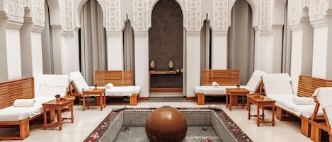A luxurious spa room with a large central fountain, multiple seating areas, and intricate wall designs.