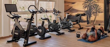 A gym with stationary bikes, a treadmill, and a wall mural.