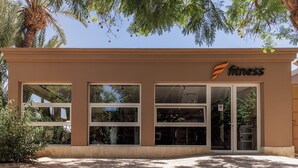 A fitness center with large windows, a palm tree, and a clear sky.