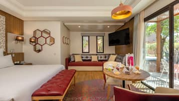 A hotel room with a bed, a sofa, a dining table with chairs, a TV mounted on the wall, and a window with a view of the outdoors.