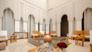 A spacious room with a large, ornate coffee table, several seating areas, and a decorative rug.