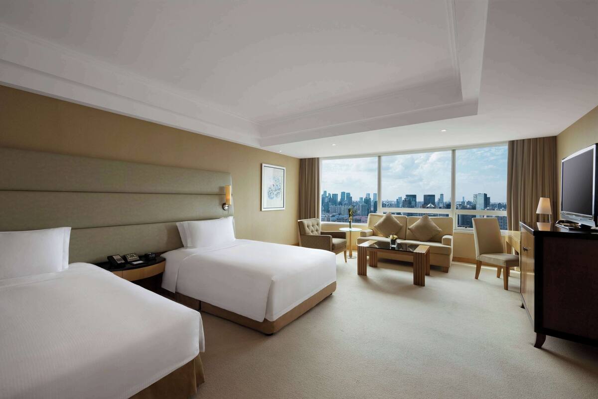 A hotel room with two beds, a sofa, a coffee table, a TV, and a city view.