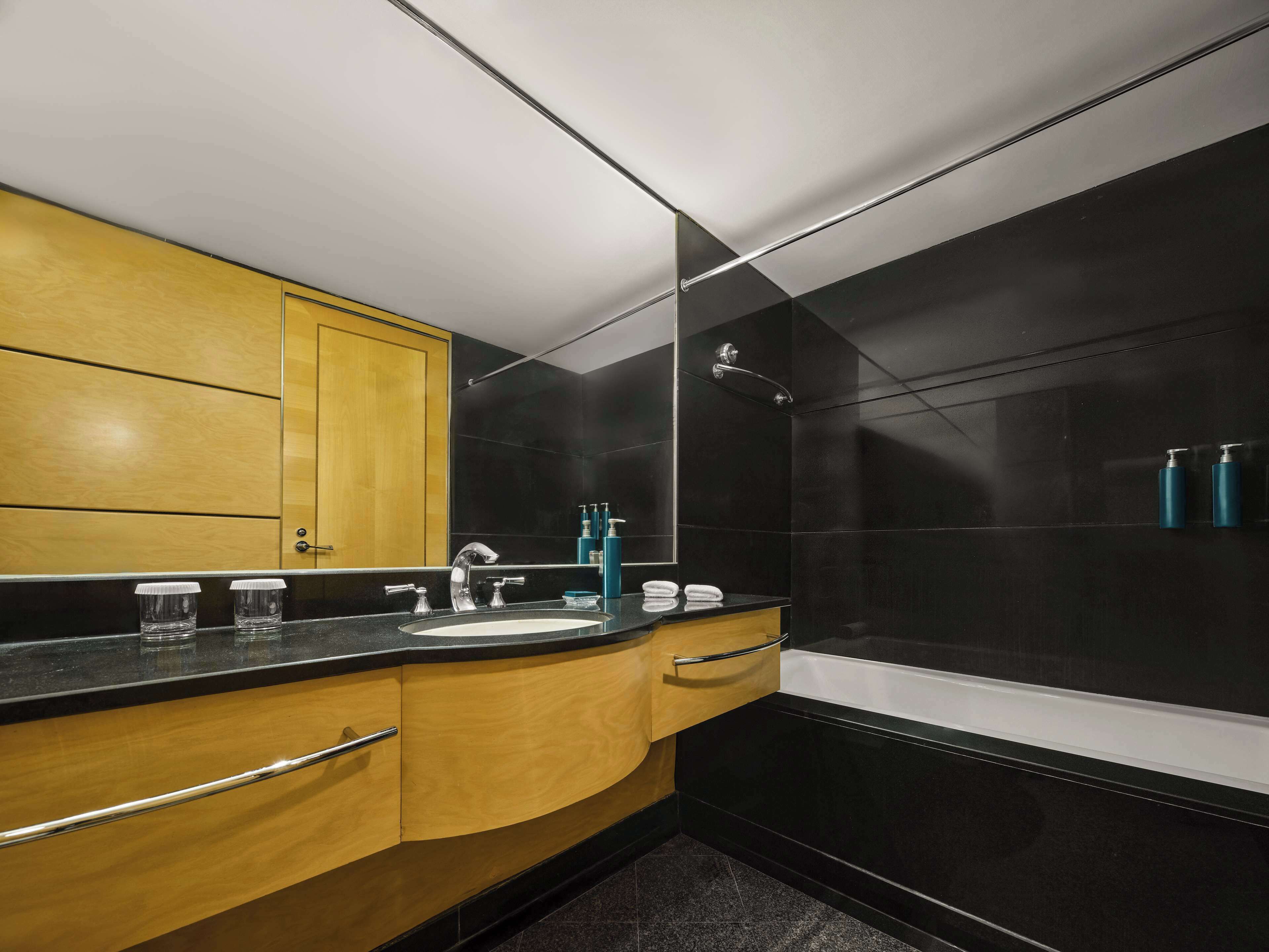 Une salle de bain moderne aux couleurs noir et or, comprenant un lavabo, un miroir et une baignoire.