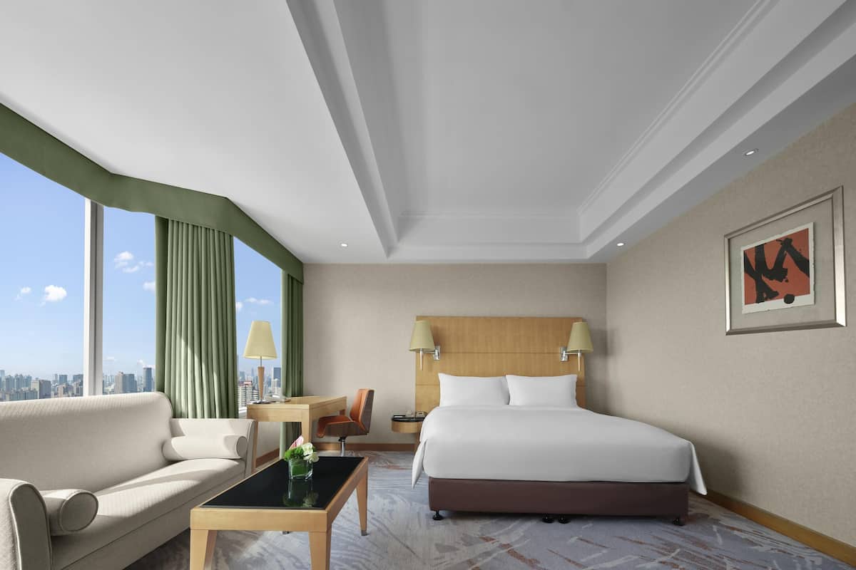 A hotel room with a bed, a sofa, a desk, a chair, and a view of the city skyline.