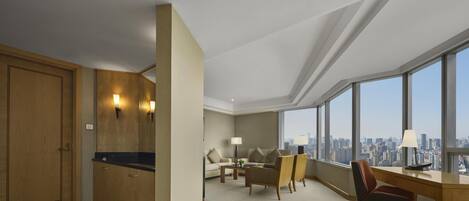 A hotel room with a city view, a desk, a chair, a sofa, and a wardrobe.