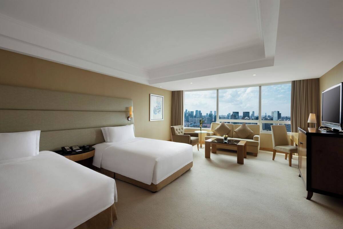 A hotel room with two beds, a sofa set, a TV, and a city view.