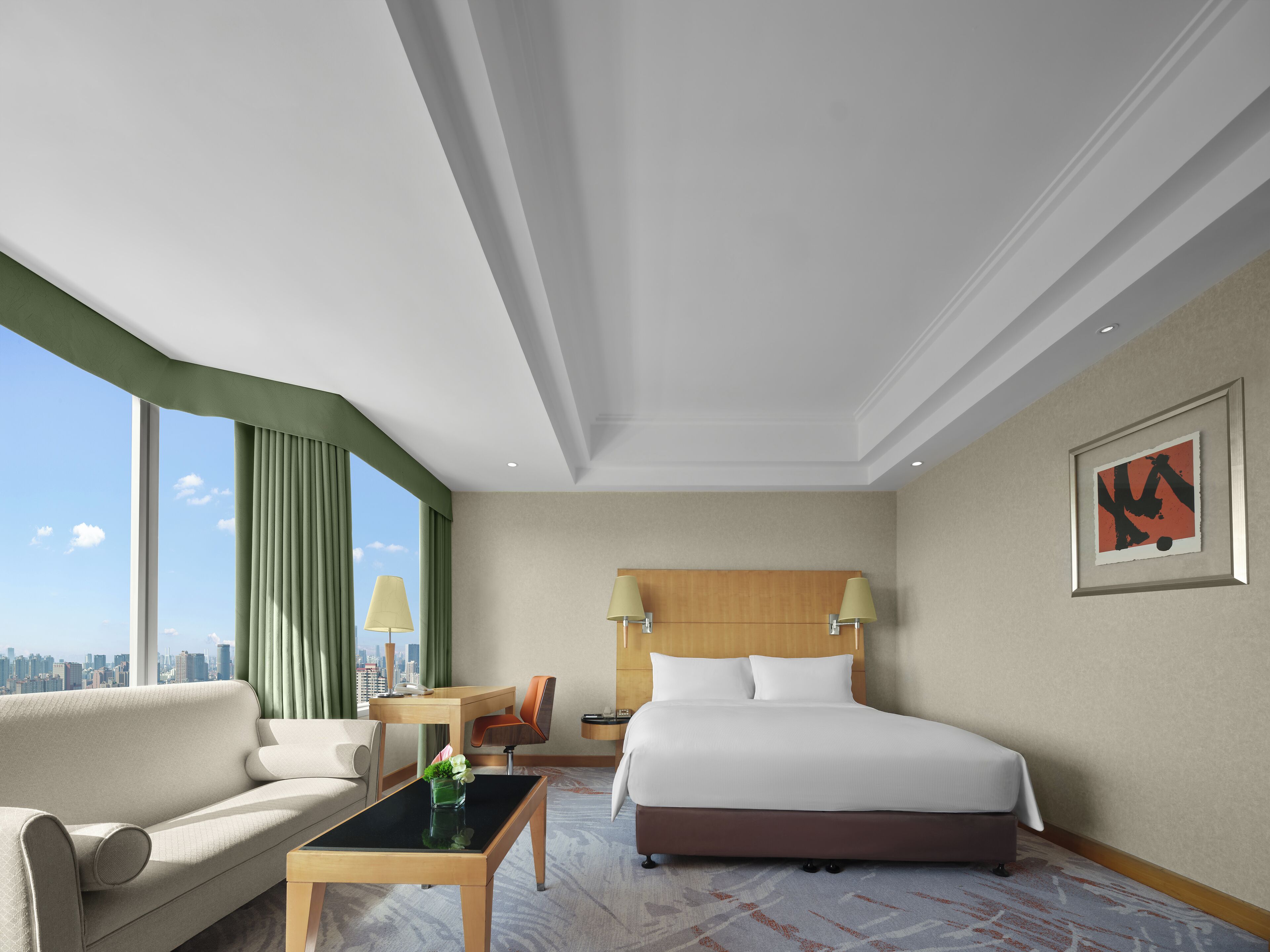 A hotel room with a bed, a sofa, a desk, and a view of the city.