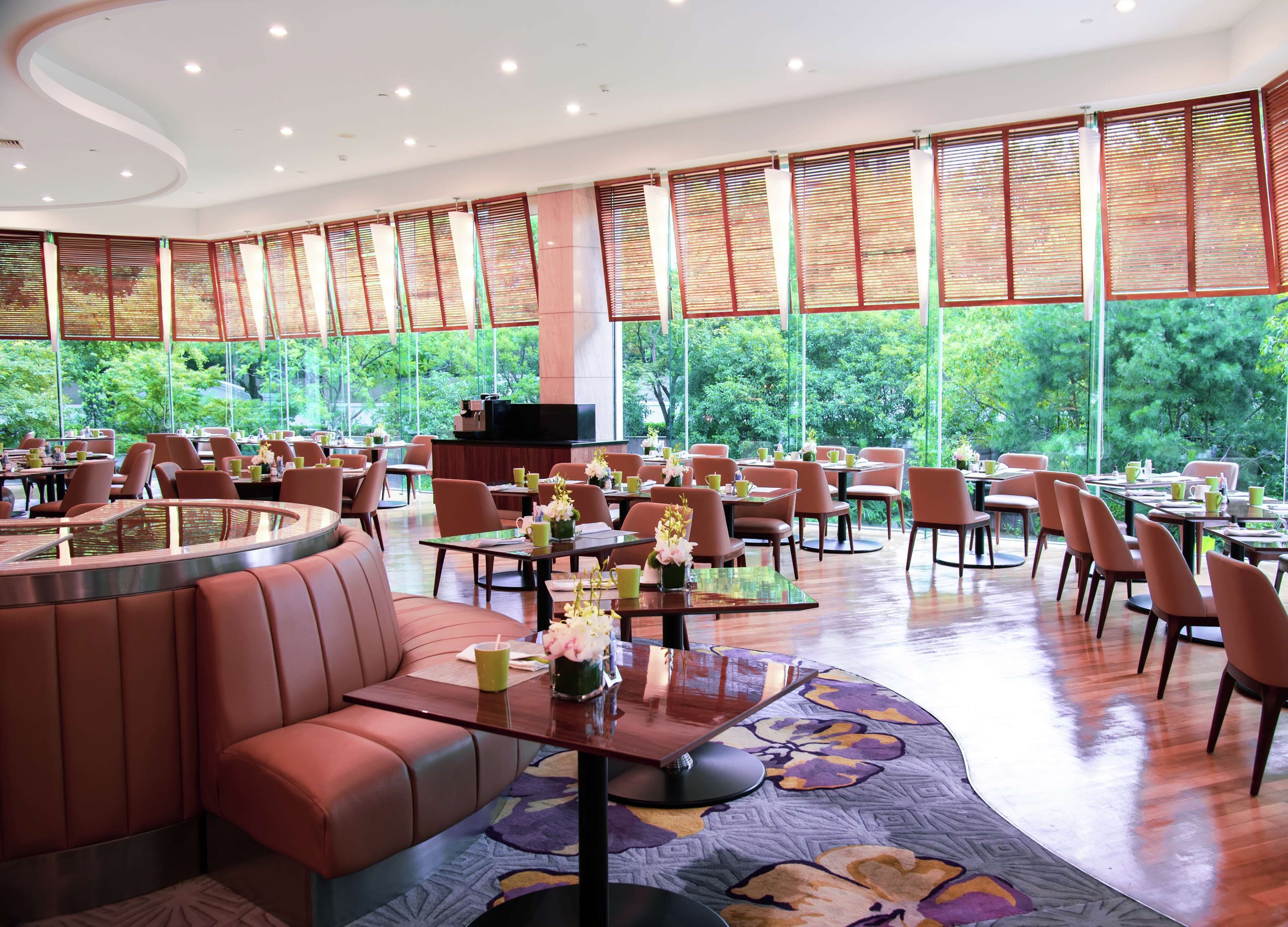 Un vaste espace de restauration intérieur, doté de nombreuses tables et de banquettes, de grandes fenêtres équipées de stores et d’un téléviseur posé sur un meuble.