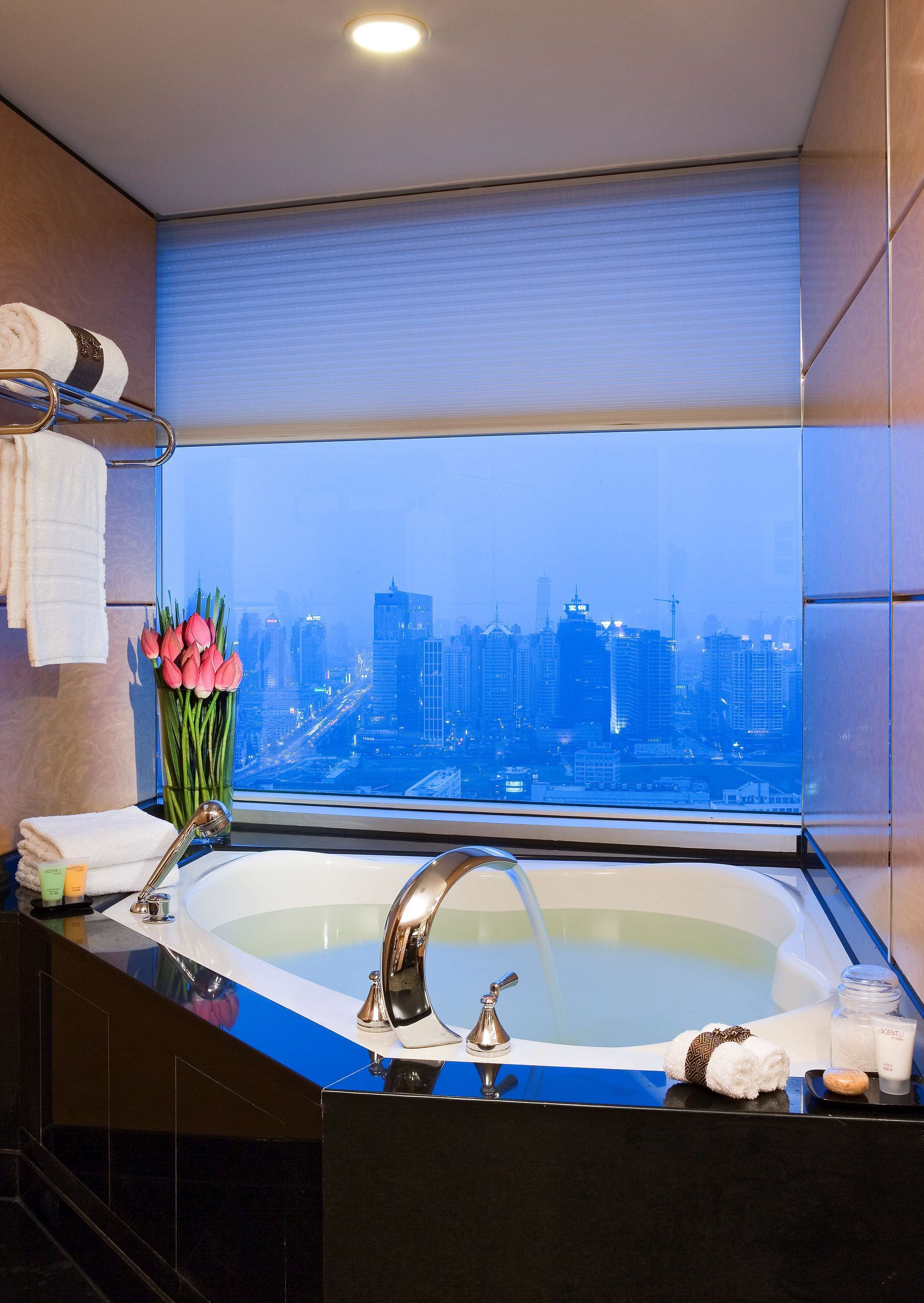 A modern bathroom with a large bathtub, a window with a city view, and toiletries on the counter.
