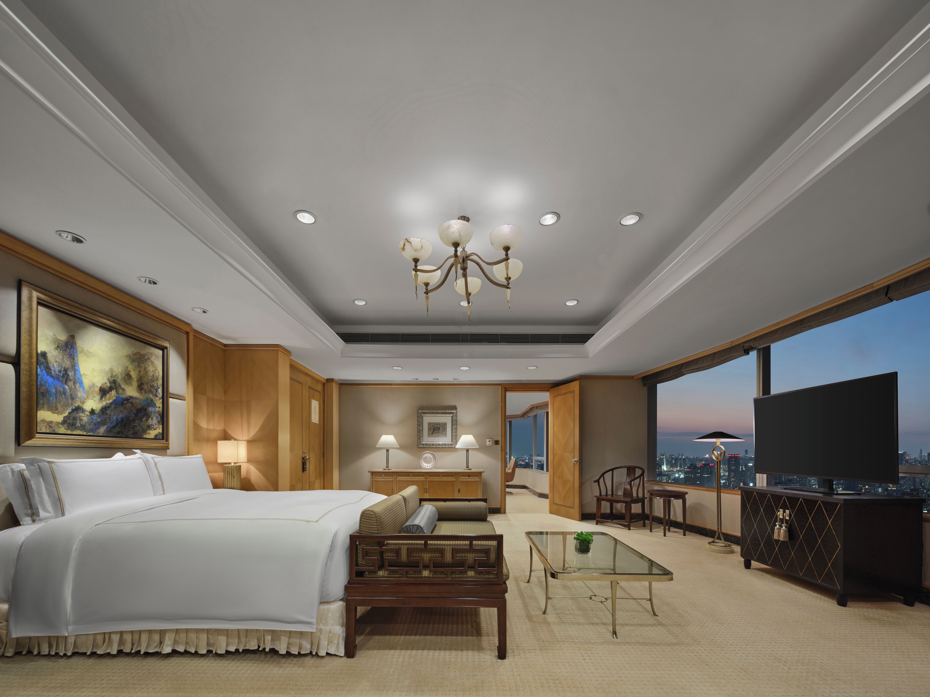 Ein modernes Hotelzimmer mit einem großen Bett, einer Sitzecke, einem Glastisch und Blick auf die Stadt.