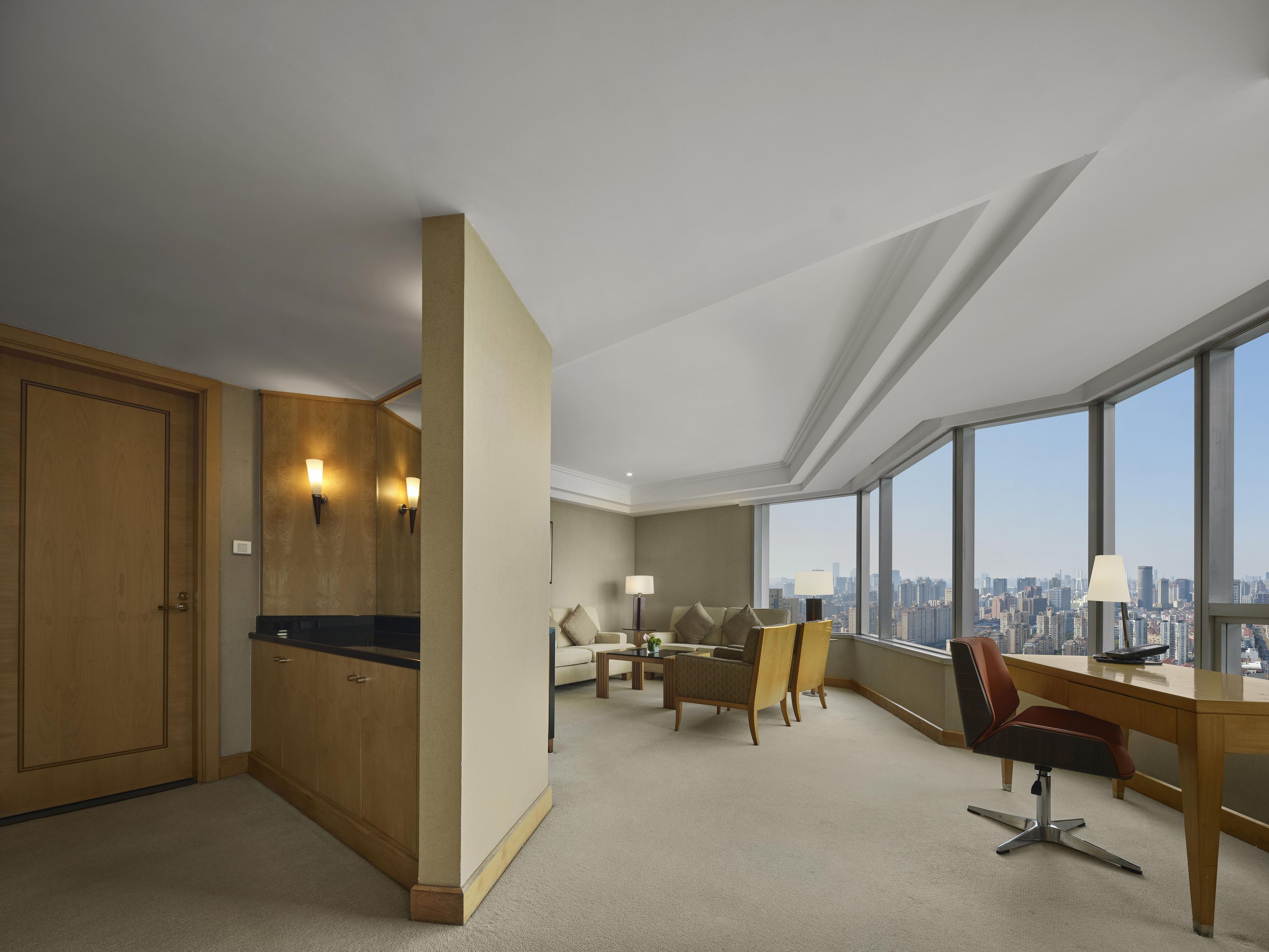 A hotel room with a city view, a desk, a chair, a sofa, and a wardrobe.