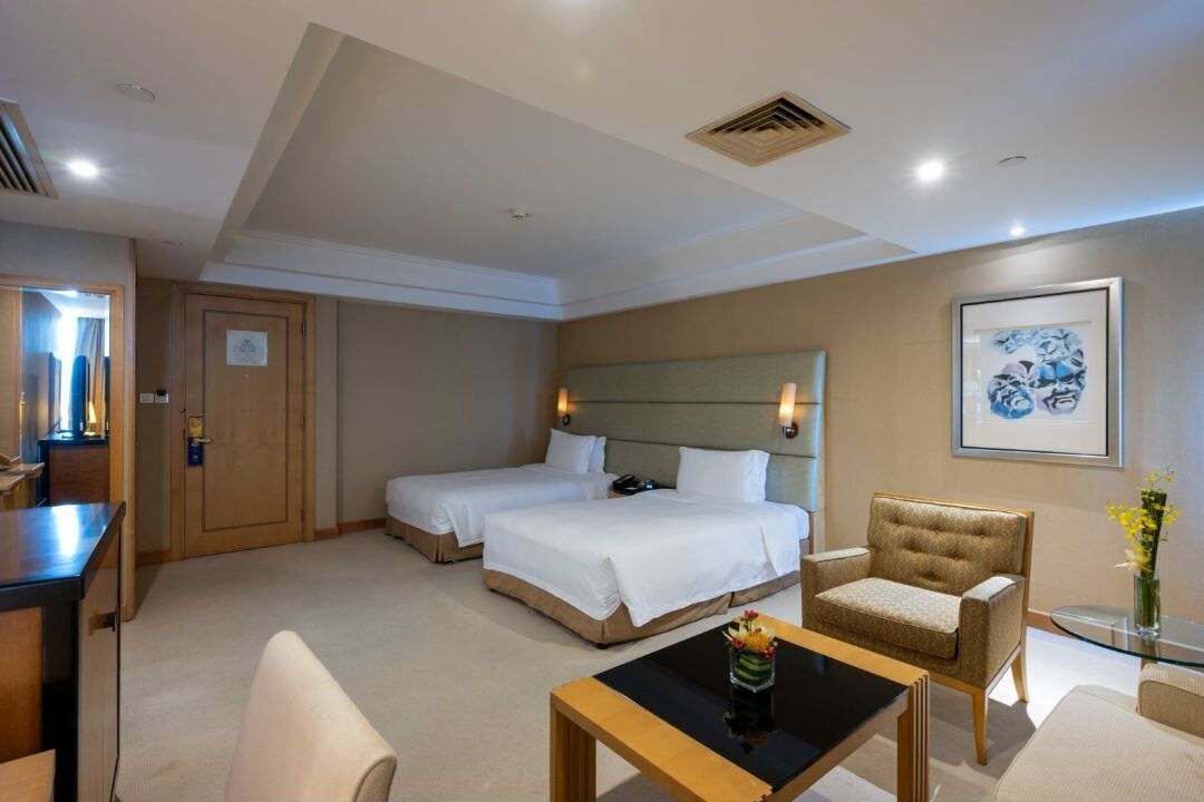 Une chambre d’hôtel avec deux lits, un bureau, une chaise et une petite table sur laquelle est posé un vase de fleurs.