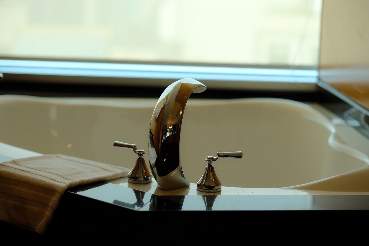 A modern bathroom with a large bathtub, two faucets, and a towel on the side.