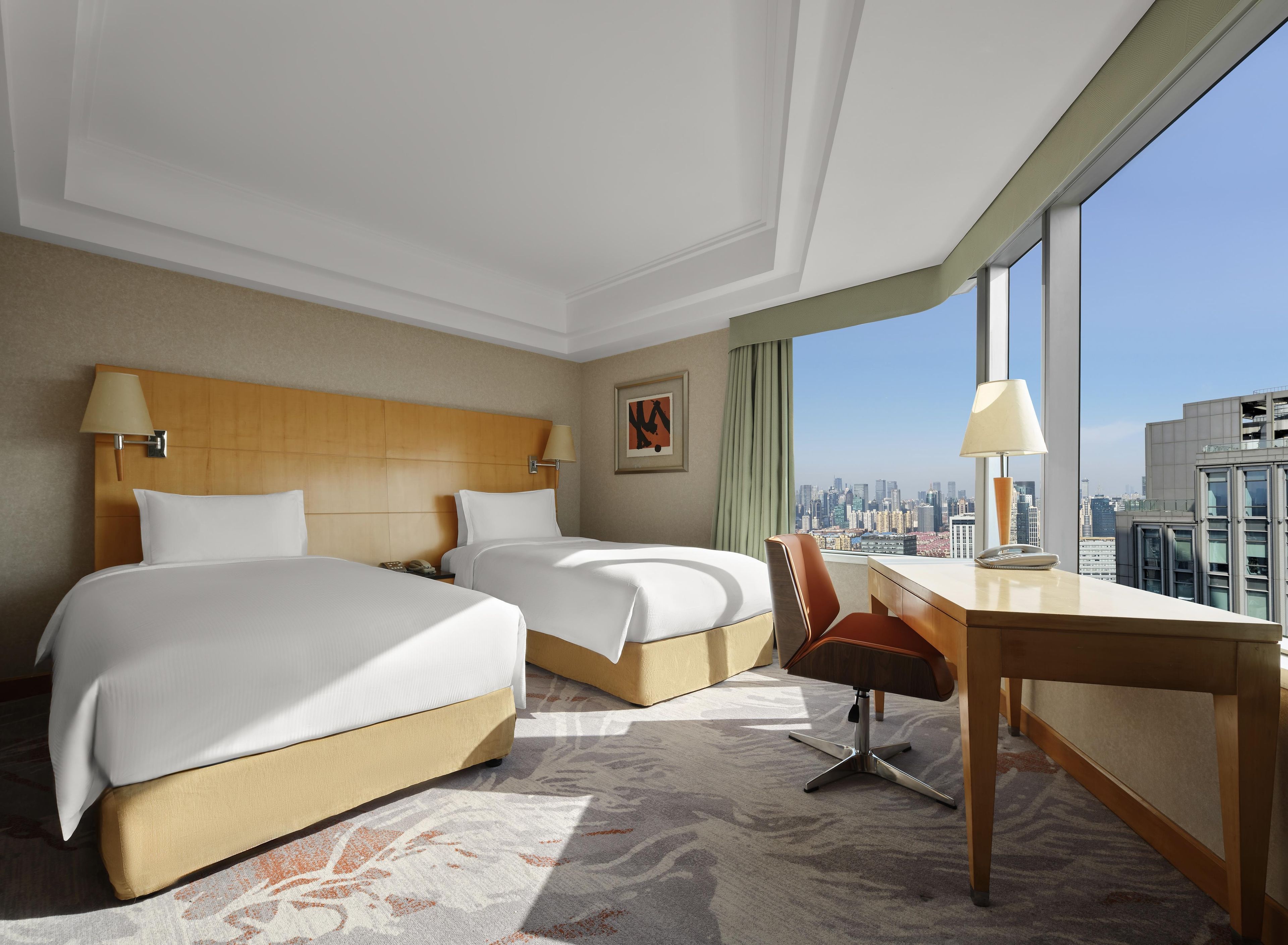 Une chambre d’hôtel avec deux lits, un bureau, une chaise et une vue sur la ville.