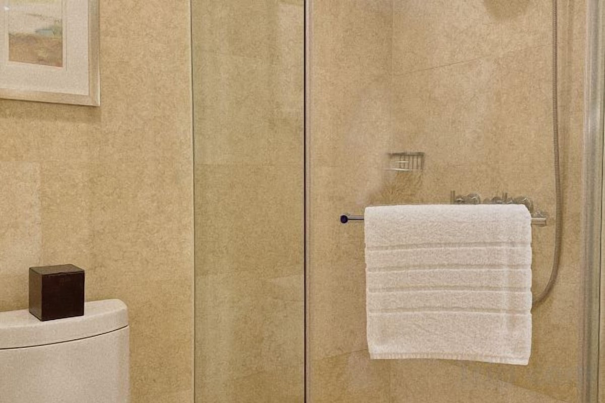 A glass-enclosed shower stall with a white towel hanging on a metal towel rack.