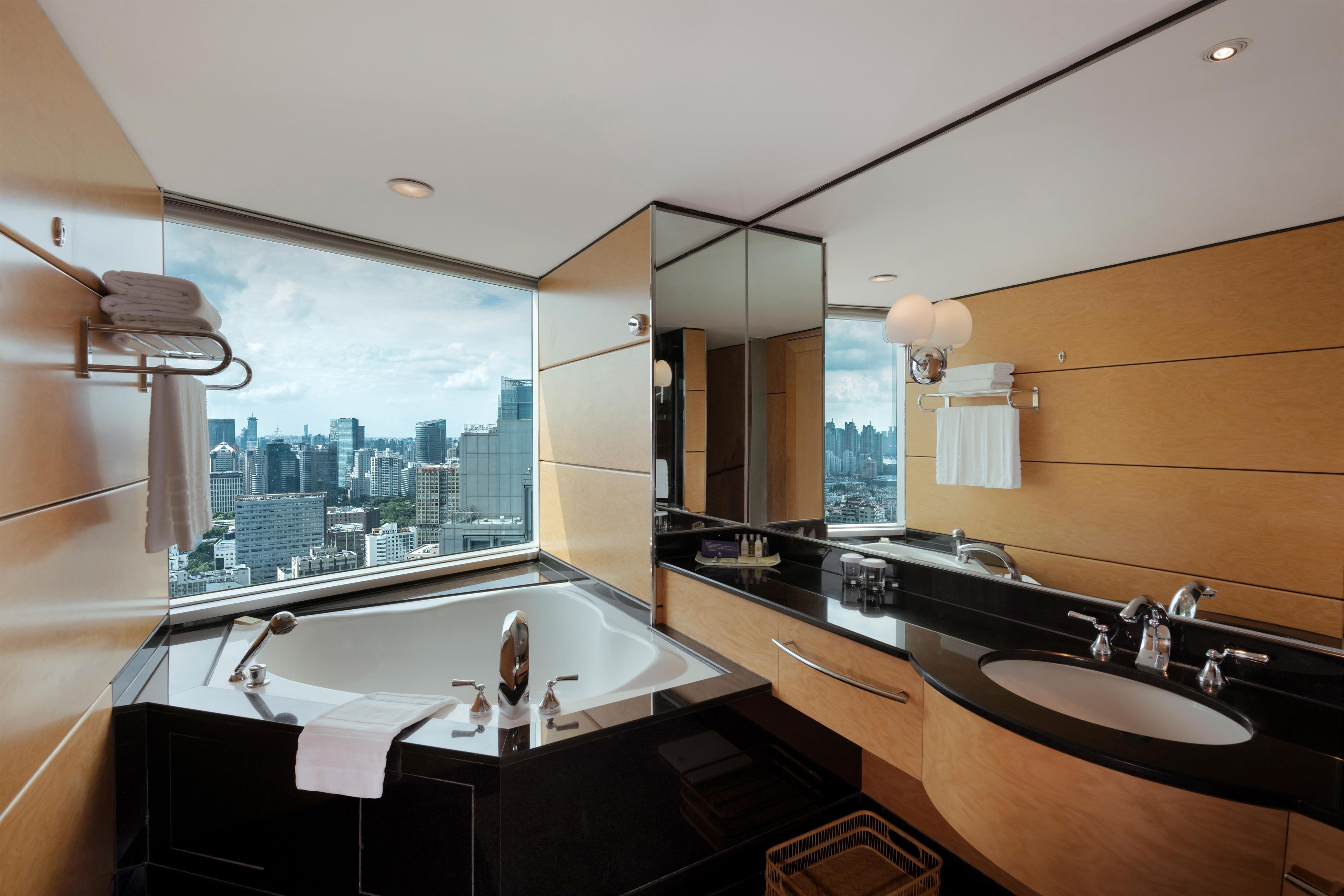 A modern bathroom with a large bathtub, two sinks, and a city view.