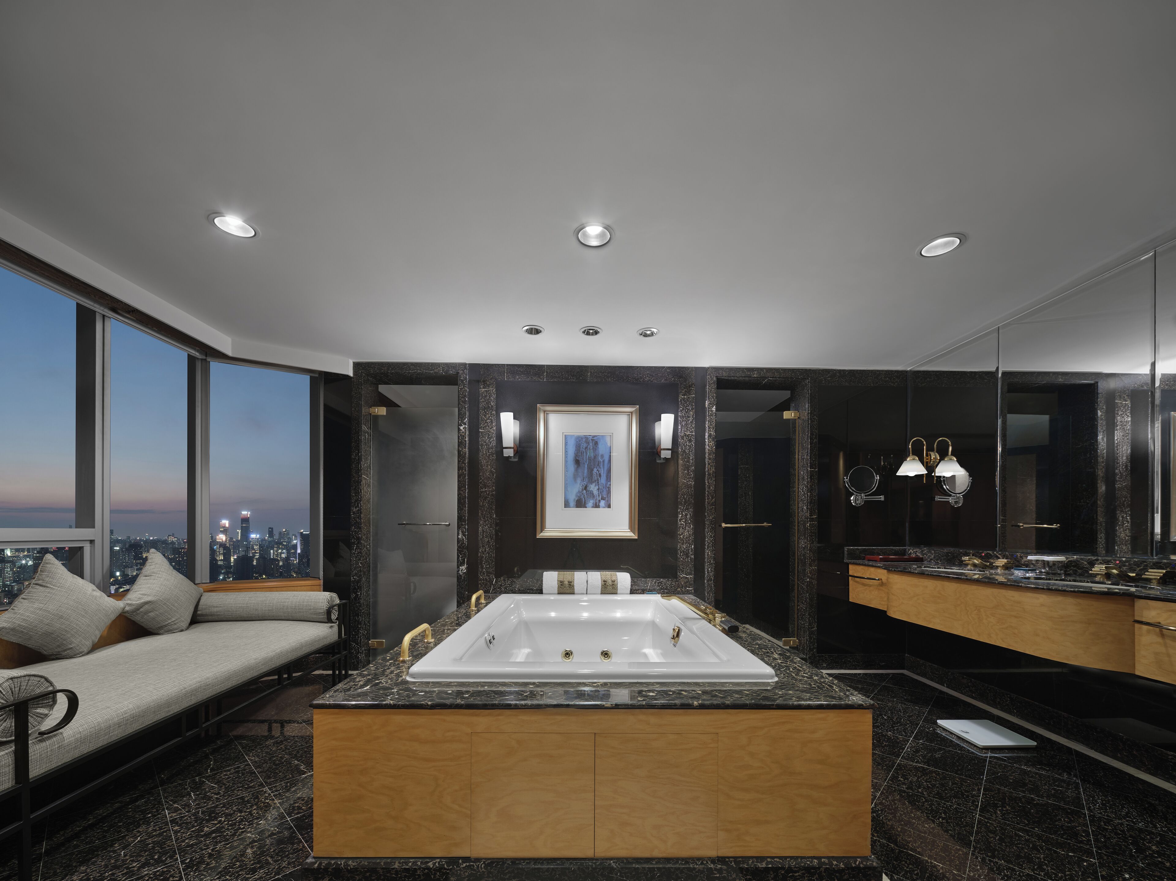 A modern bathroom with a large bathtub, a vanity with a mirror, and a city view.