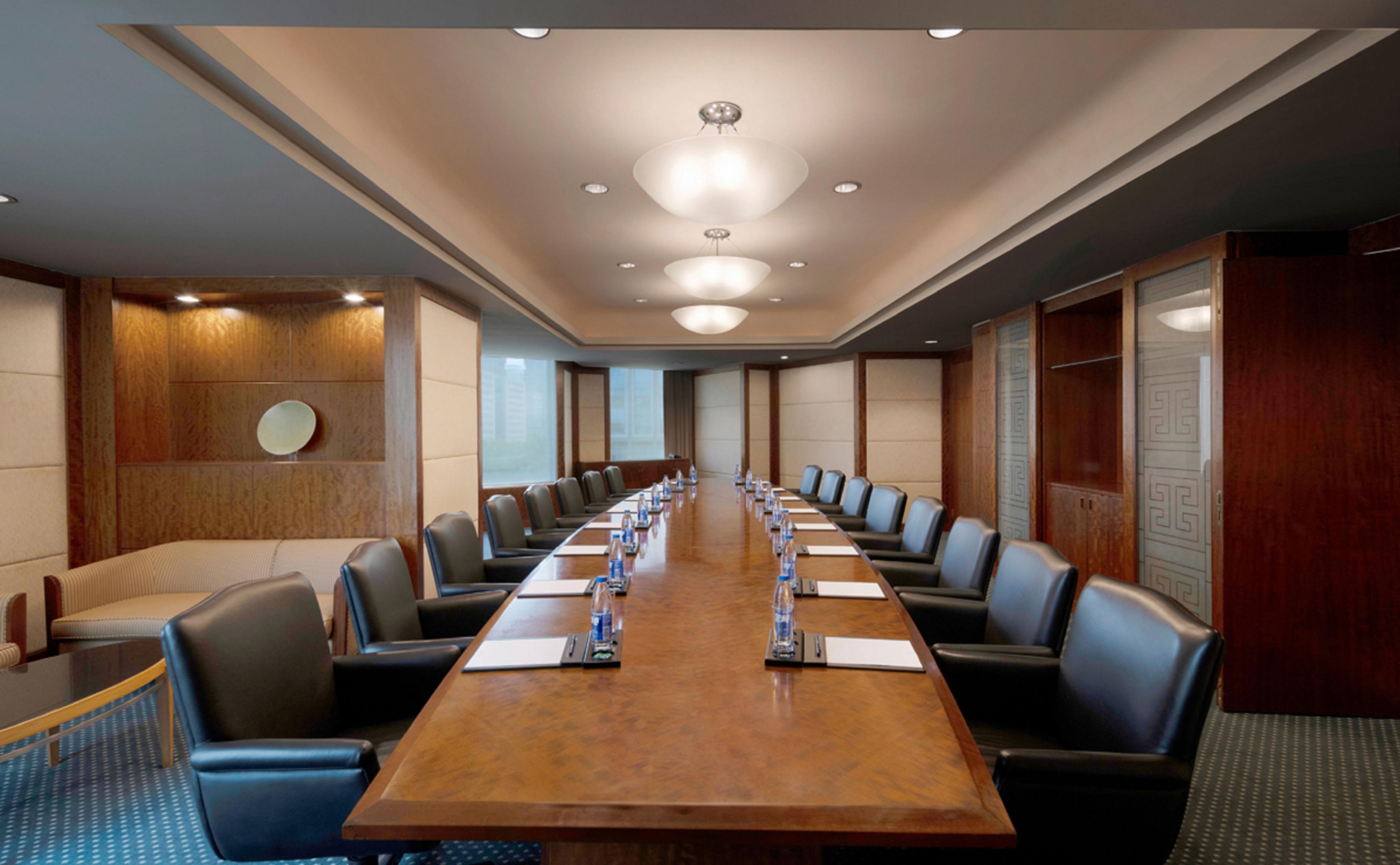 A conference room with a long table, chairs, and a wooden panel wall.