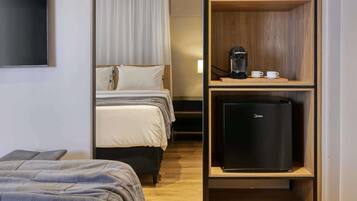 A hotel room with a bed, a desk with a coffee machine, and a refrigerator.