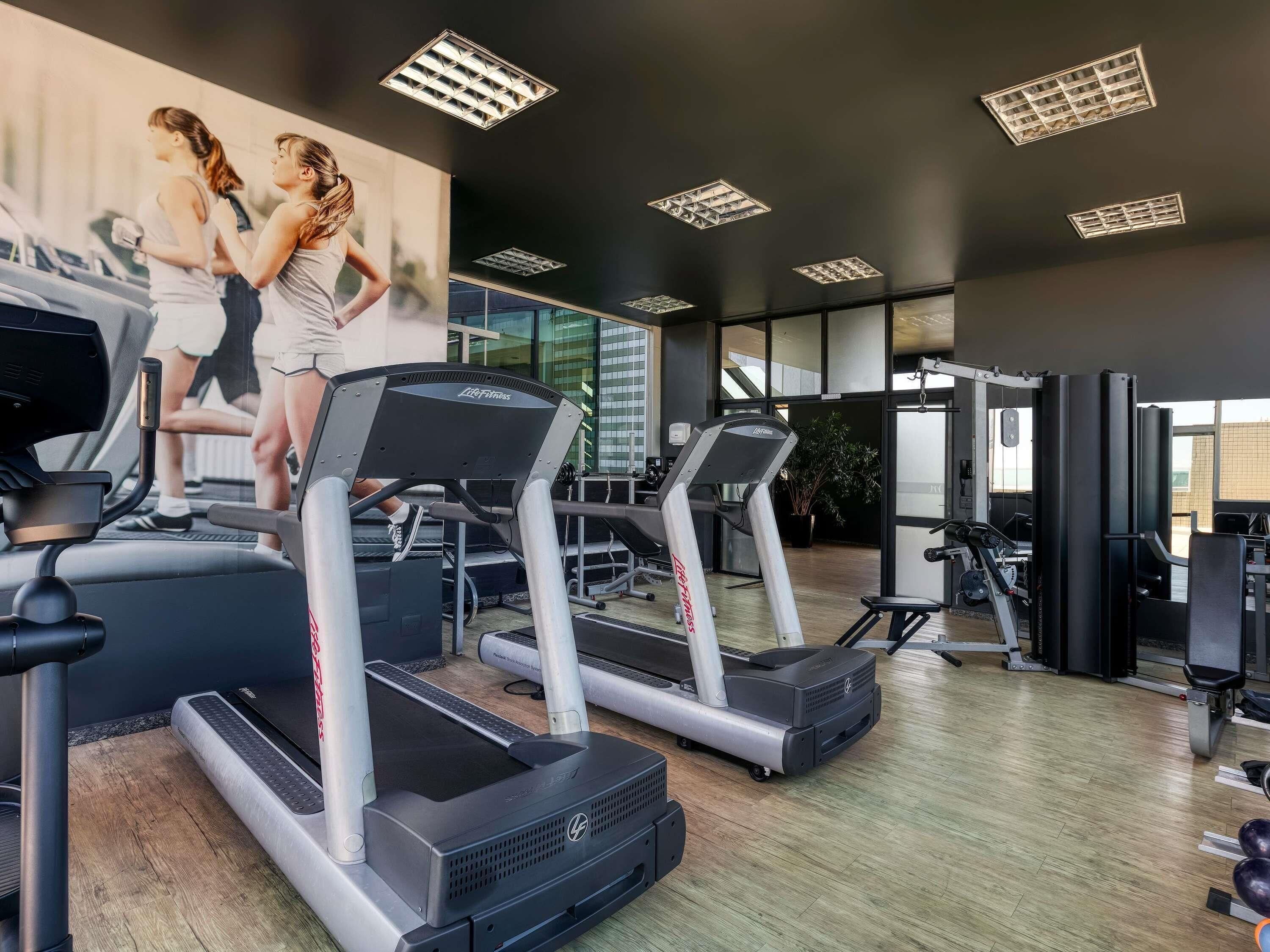 A gym with treadmills, weight machines, and a large mirror wall.