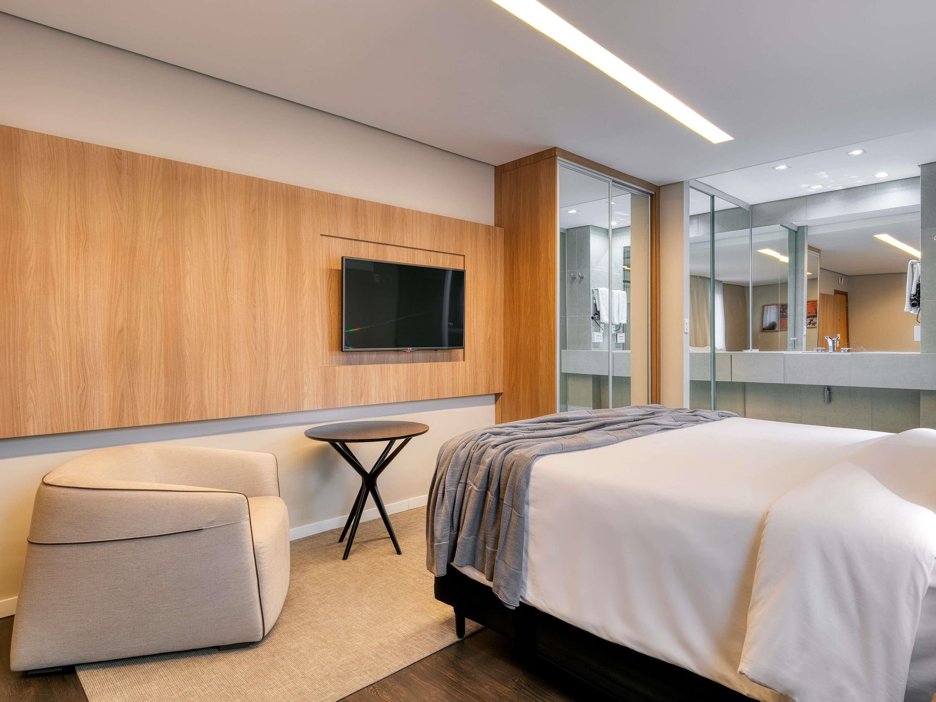 Une chambre d’hôtel moderne dotée d’un grand lit, d’un coin salon, d’un téléviseur fixé au mur et d’un grand miroir.
