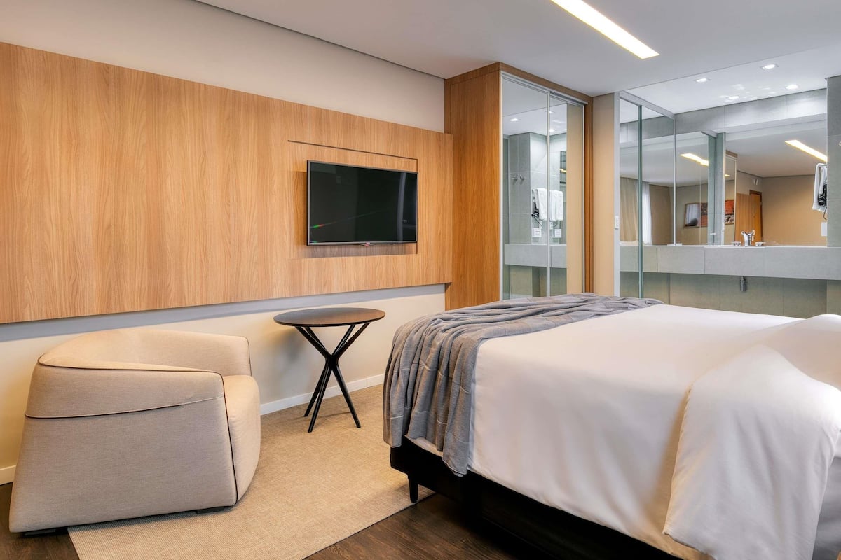 Une chambre d’hôtel moderne dotée d’un grand lit, d’un coin salon, d’un téléviseur fixé au mur et d’un grand miroir.