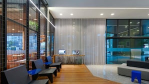 A modern waiting area with wooden flooring, seating, and a glass partition with a view.