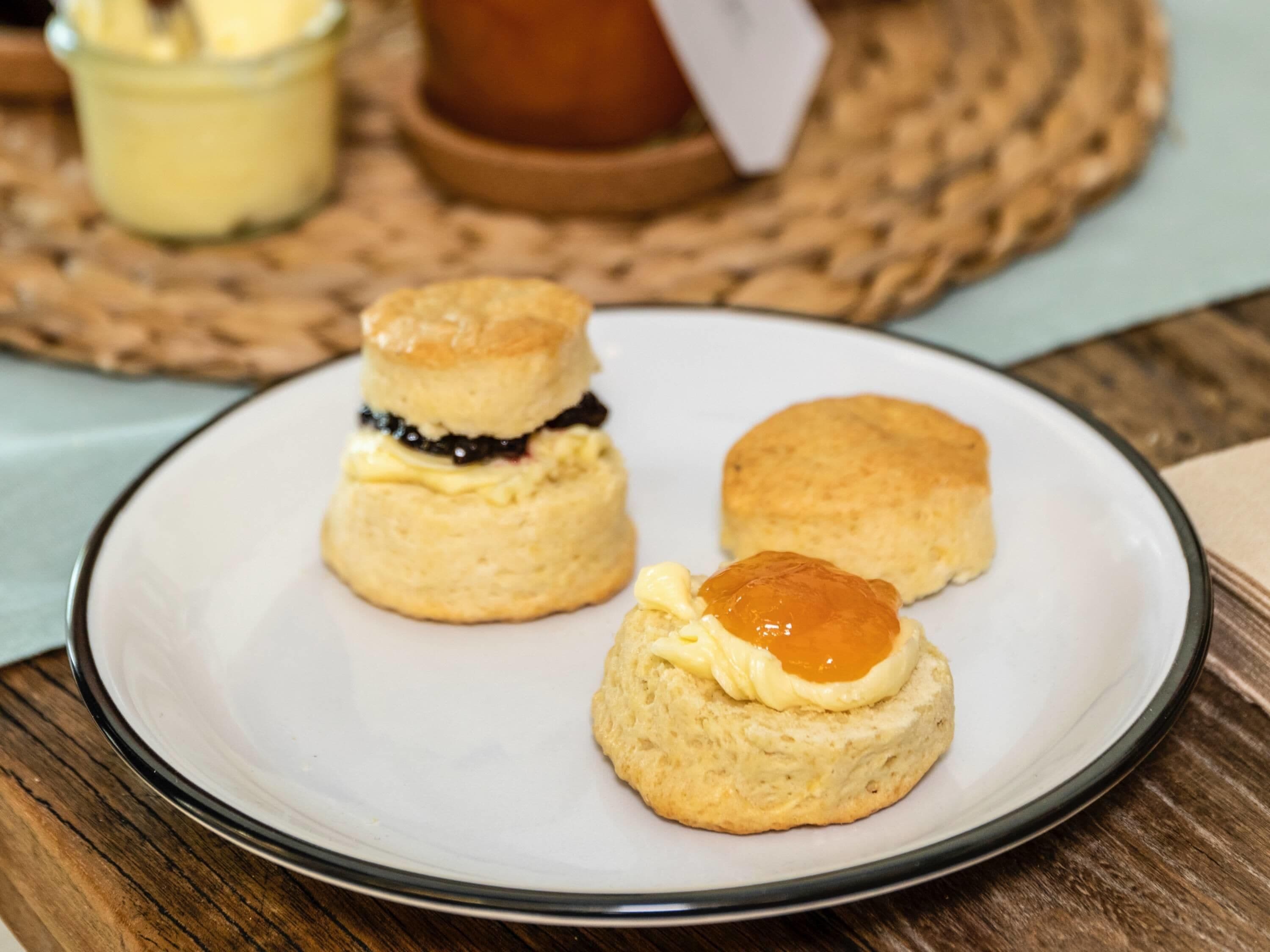 A plate with three scones, one with jam and one with butter.
