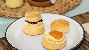 A plate with three scones, one with jam and one with butter.