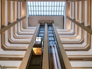A modern interior with a central escalator flanked by geometric wall designs and a skylight above.