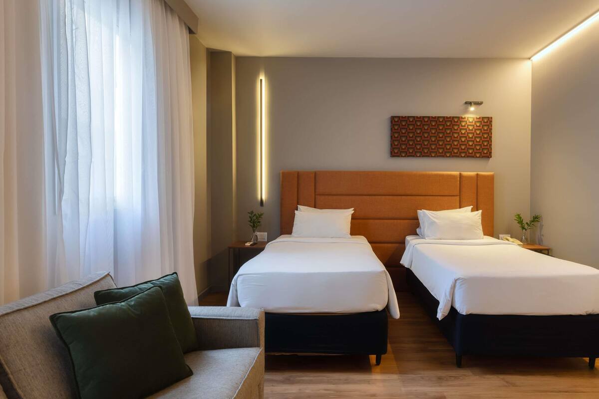 Une chambre d’hôtel avec deux lits, un canapé, une lampe fixée au mur et un panneau décoratif.