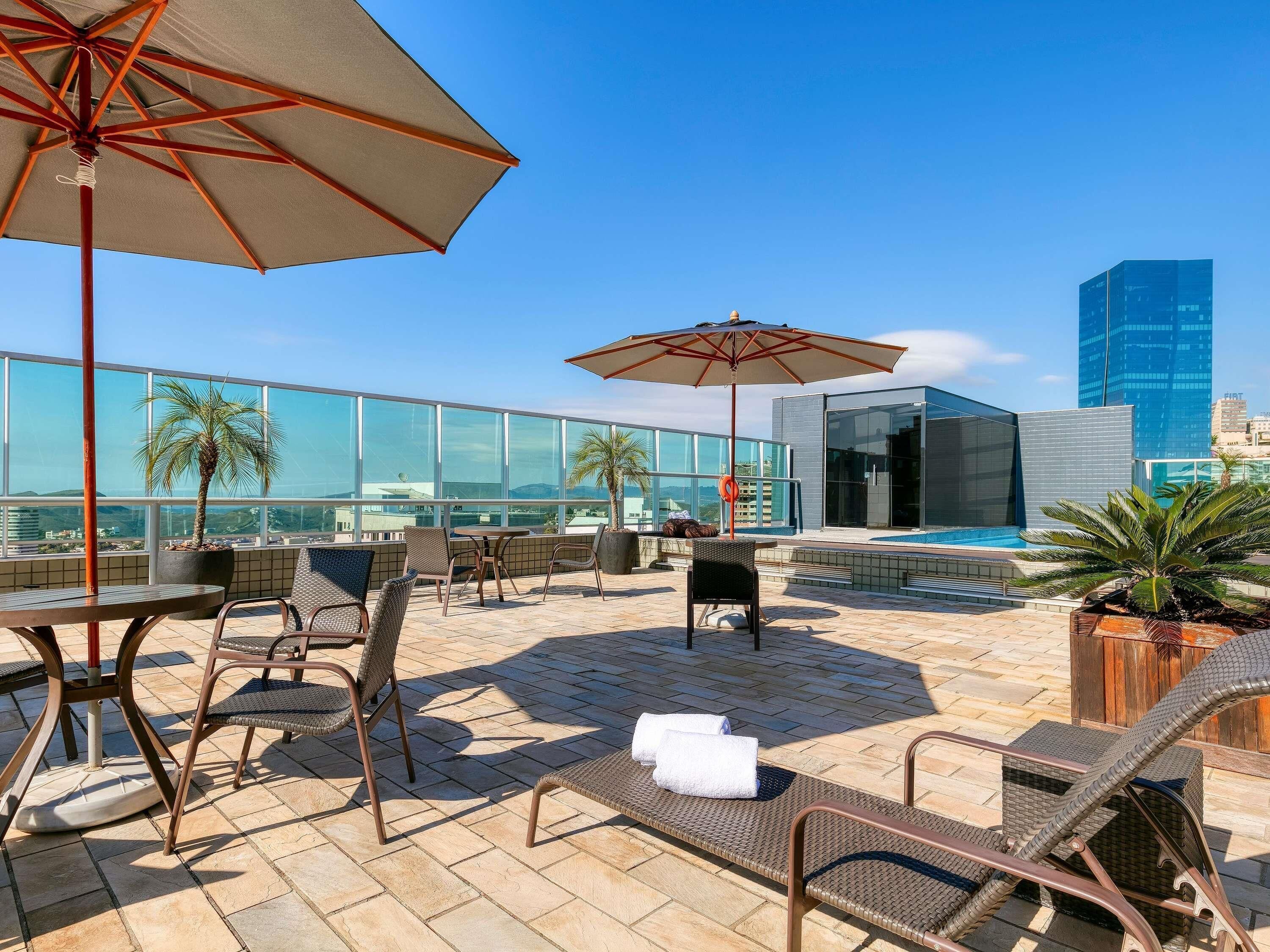 Terraza en la azotea con mobiliario exterior, sombrillas y vistas a edificios modernos.