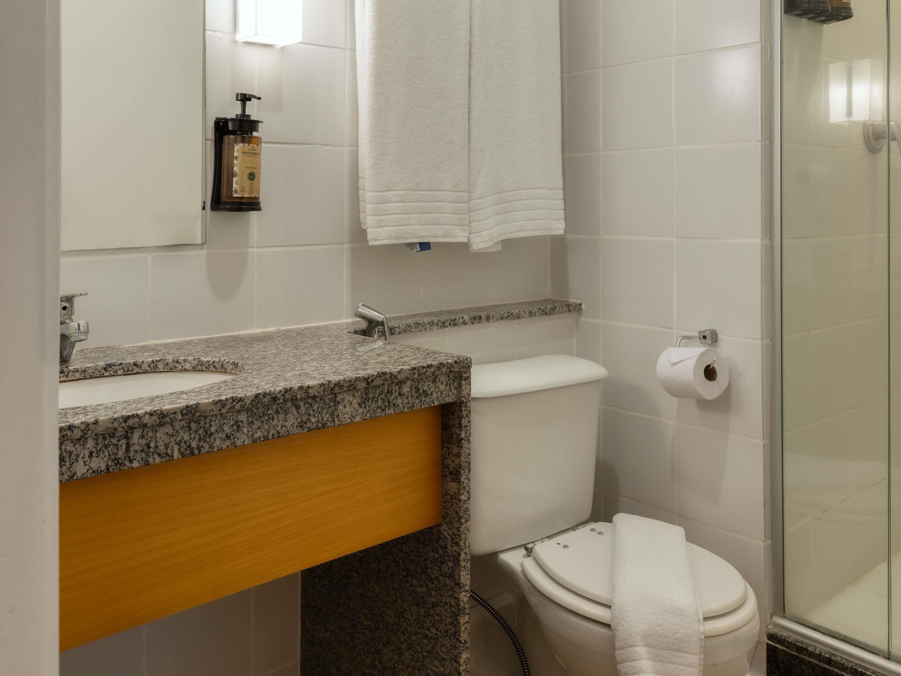 A bathroom with a granite countertop, a white toilet, a glass shower enclosure, and a towel rack.