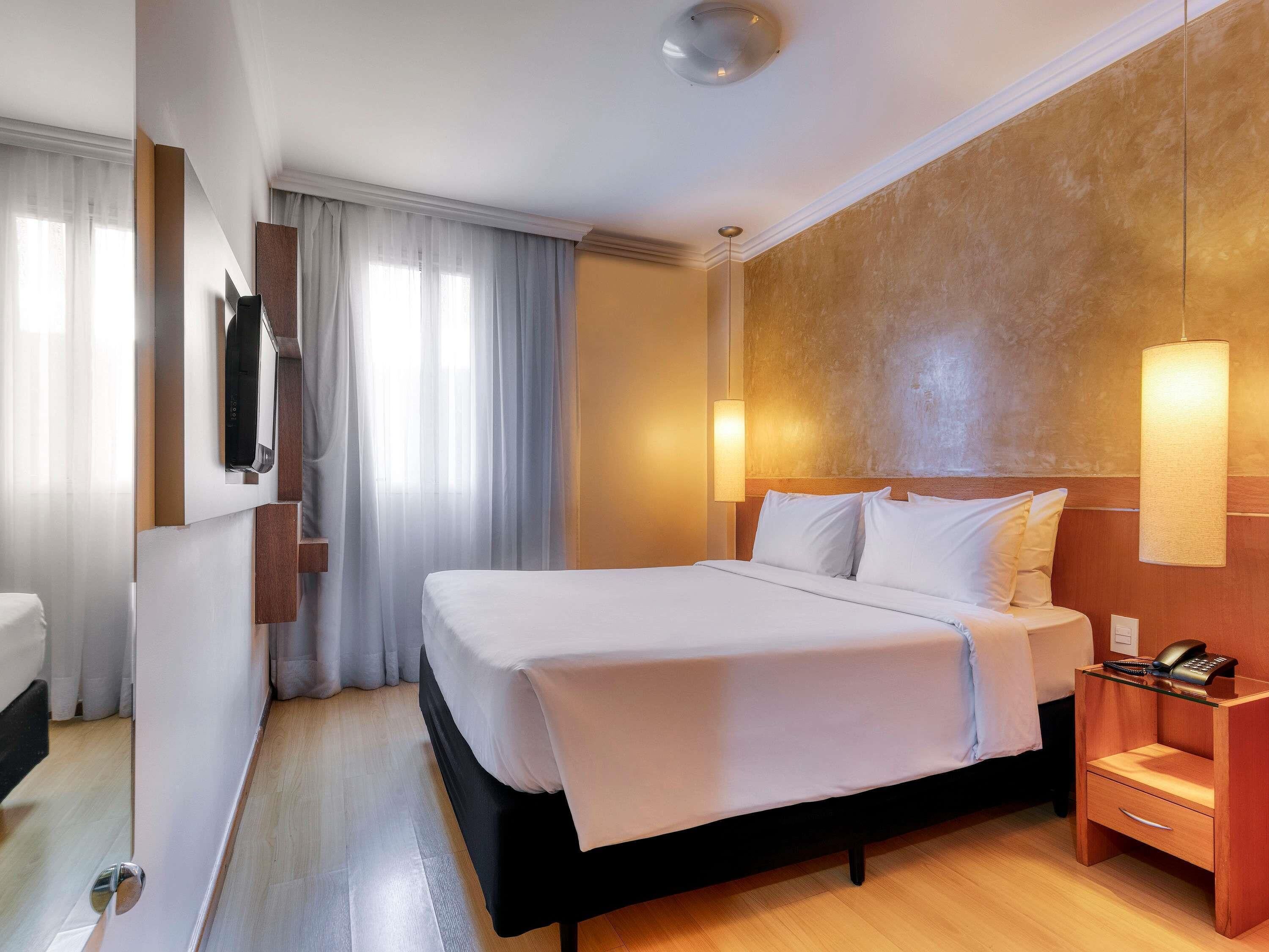A hotel room with a bed, bedside table, lamp, and a mirror.