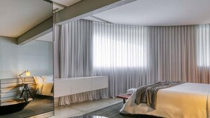 A modern hotel room with a bed, bedside table, lamp, and a large window with curtains.