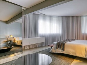 A modern hotel room with a bed, bedside table, lamp, and a large window with curtains.