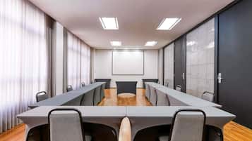 A conference room with a long table, chairs, a projector screen, and a large window with curtains.