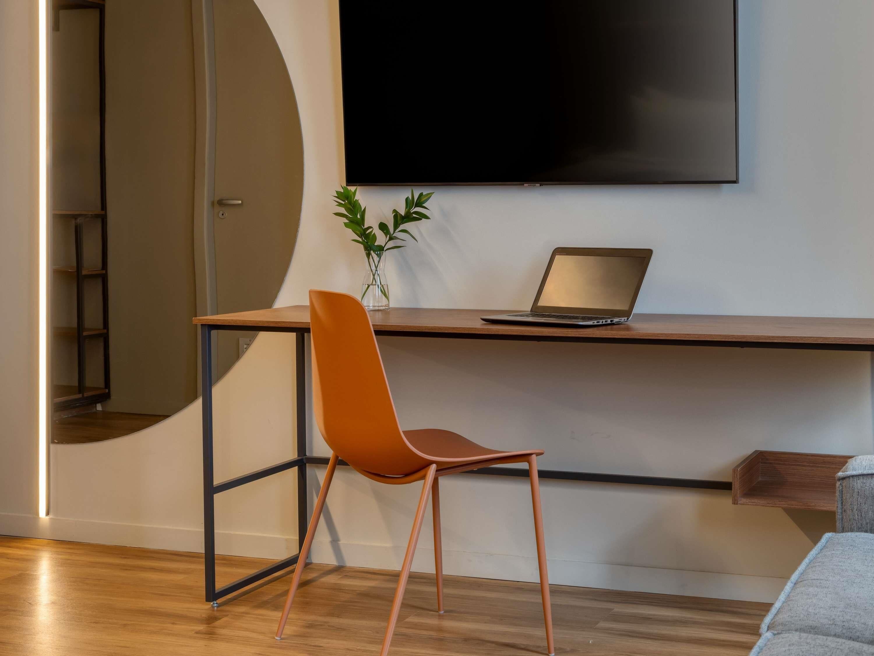 Una habitación moderna con un escritorio, una computadora portátil, una silla, un televisor y una planta.