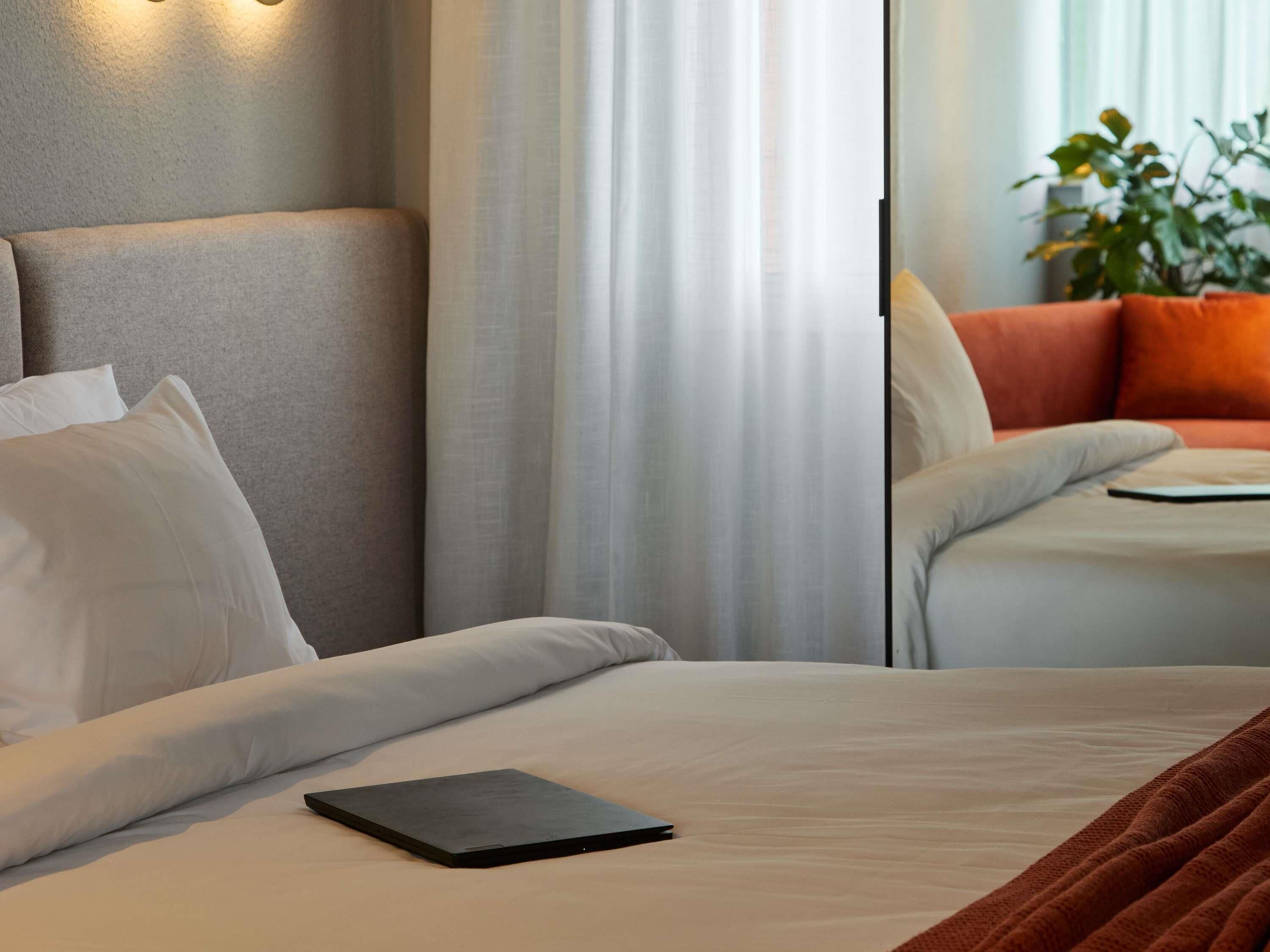 A hotel room with a bed, a bedside table, a lamp, and a plant.
