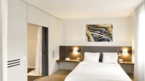 A hotel room with a large bed, bedside tables with lamps, a painting on the wall, and a wardrobe. - B&B HOTEL Paris Grand Roissy CDG Aéroport (Roissy-en-France)