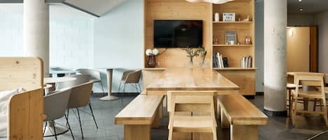 Uma sala de estar moderna e espaçosa, com uma mesa de madeira e bancos, uma TV de tela plana fixada em uma parede de madeira e uma estante com diversos objetos.